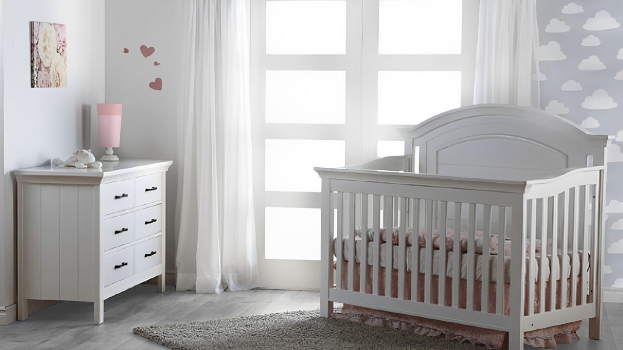 A baby's crib near a window with sheer curtains.