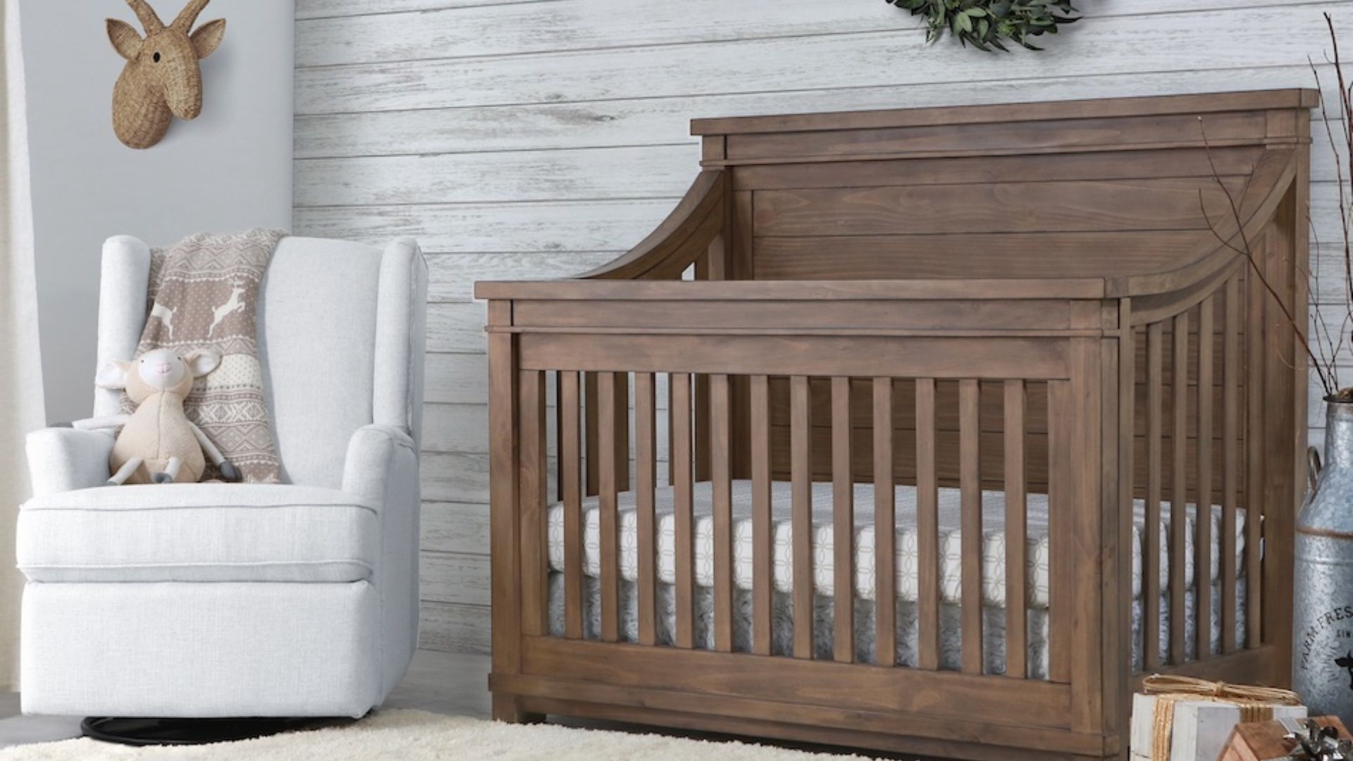 A wooden baby crib next to a white cushioned chair.